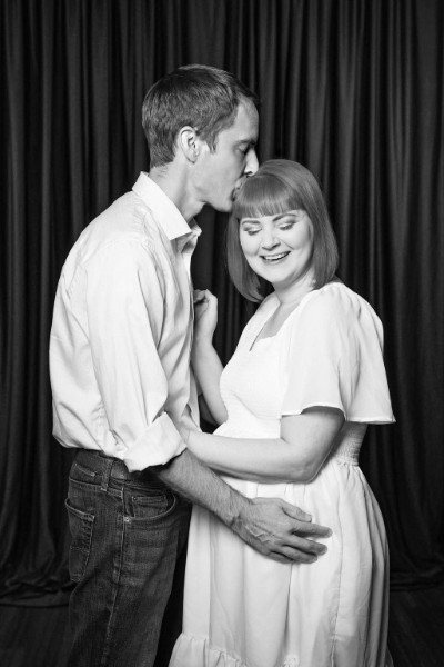 Black and white photo of Nick kissing Nirvana's forehead as they hold her bump
